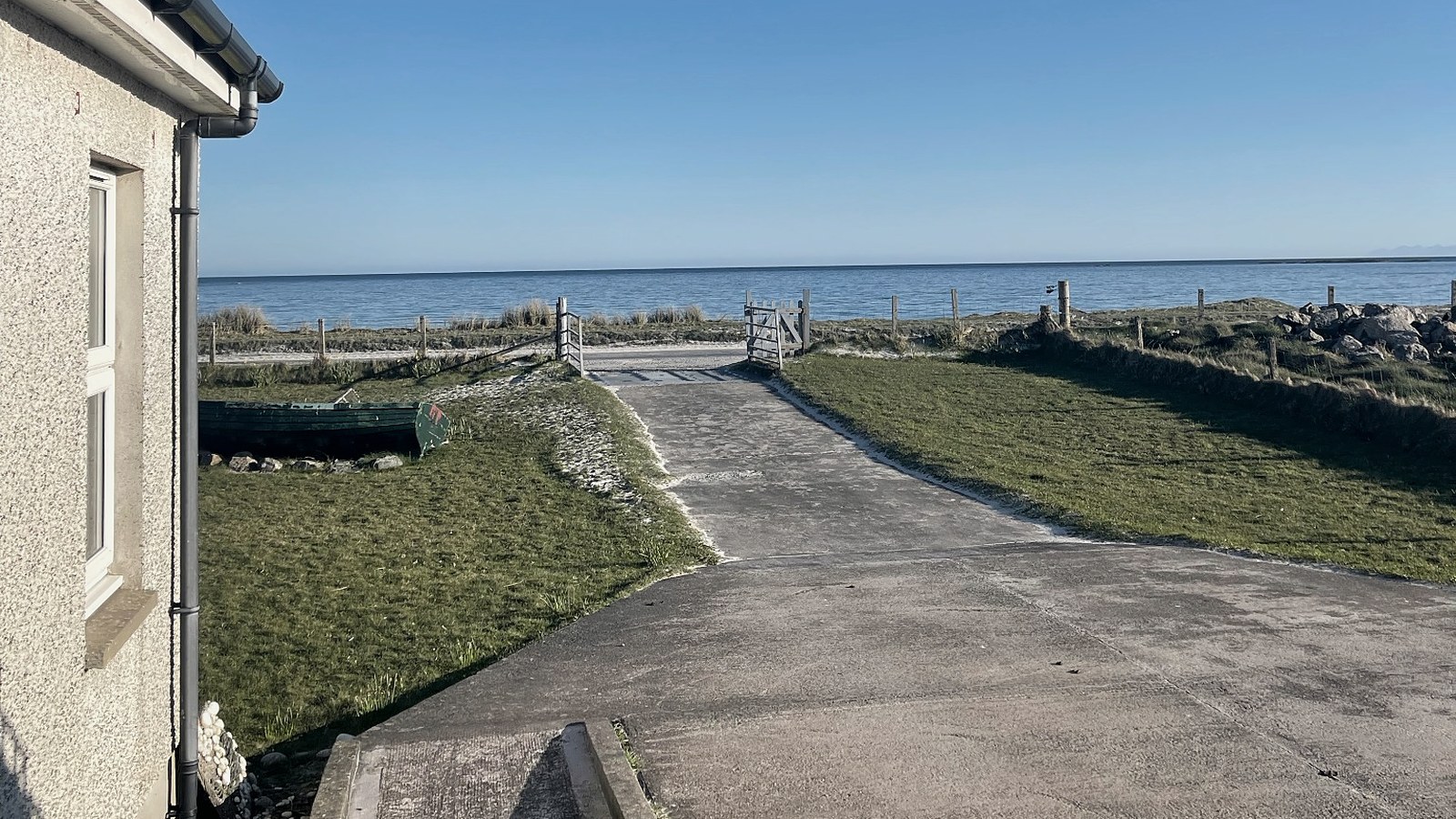 A driveway leading toward a gate, dunes and the sea beyond.
