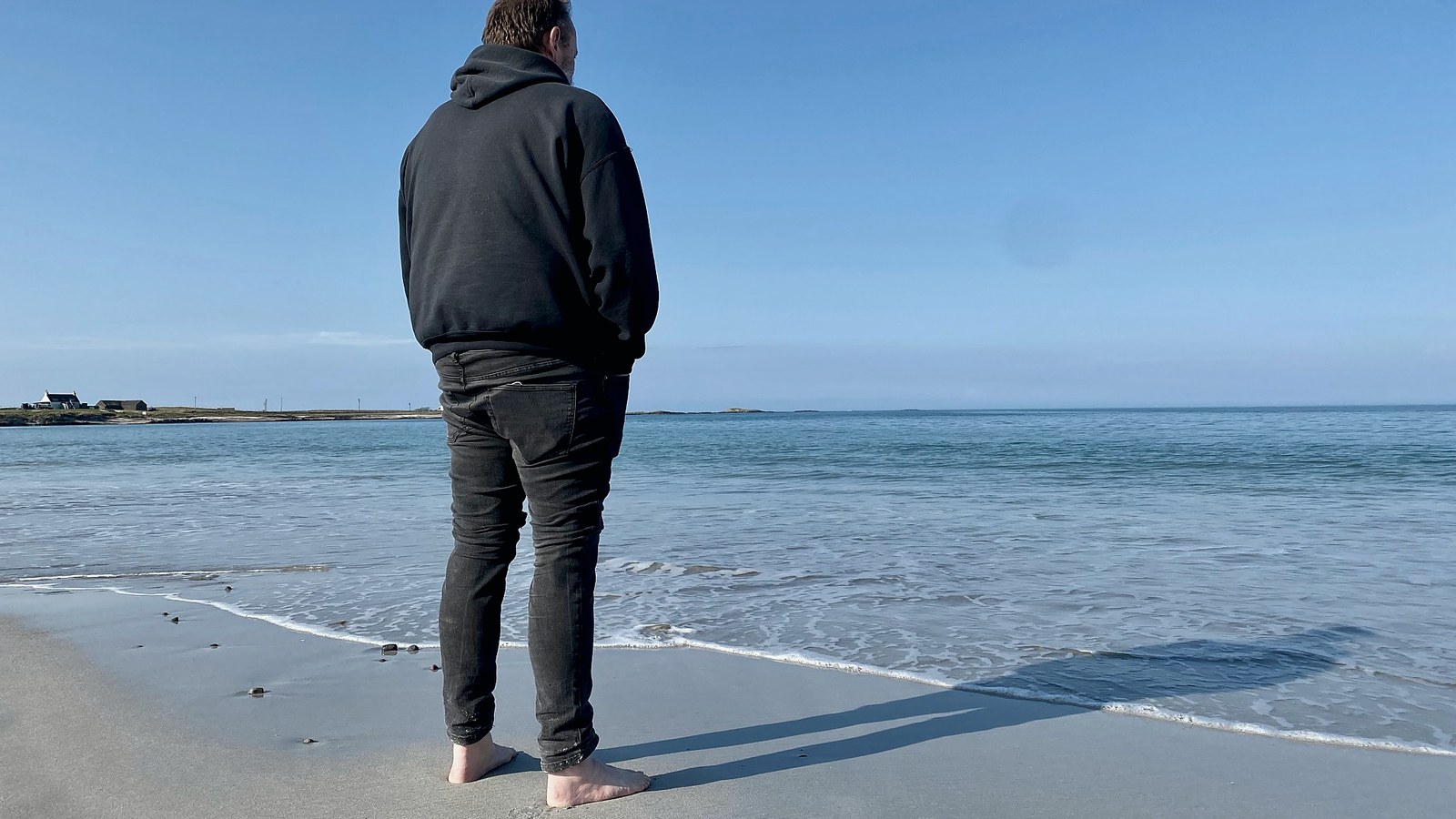 A barefoot man stands on the beach facing the Atlantic sea.